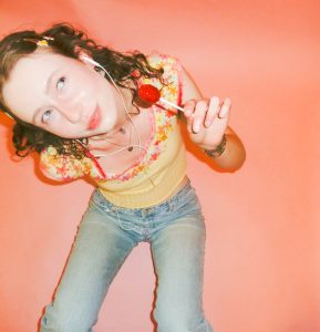 model posing with earbuds and lollipop with pink background